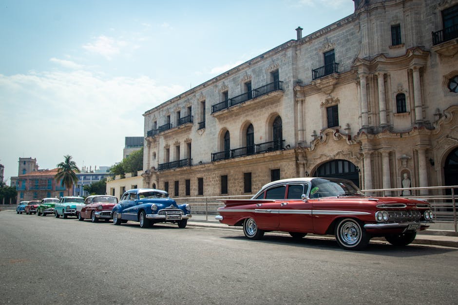 Classic American cars lined up on a picturesque street beside old Cuban architecture in Havana.