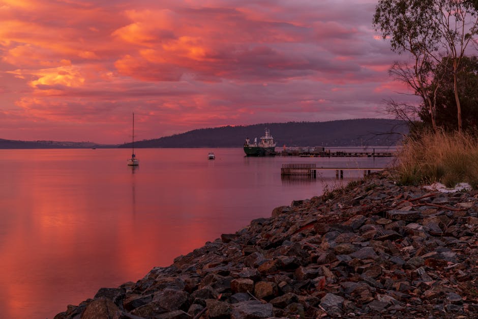 A tranquil harbor with boats and a pier at sunset, reflecting vivid colors on the water.