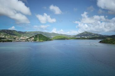 Breathtaking view of the Caribbean Sea with green hills and boats under a blue sky.
