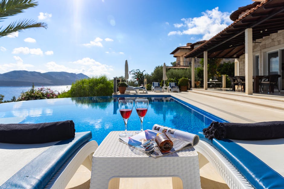 Elegant seaside villa with infinity pool, wine glasses, and stunning ocean view on a sunny day.