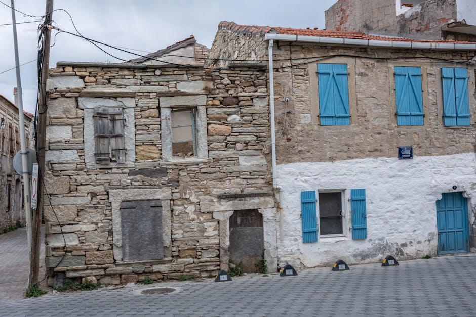 Rustic stone houses with blue shutters on a quiet street in Foça, İzmir, Türkiye.