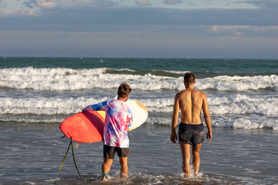 Two surfers prepare to catch waves on a sunny beach, carrying surfboards.