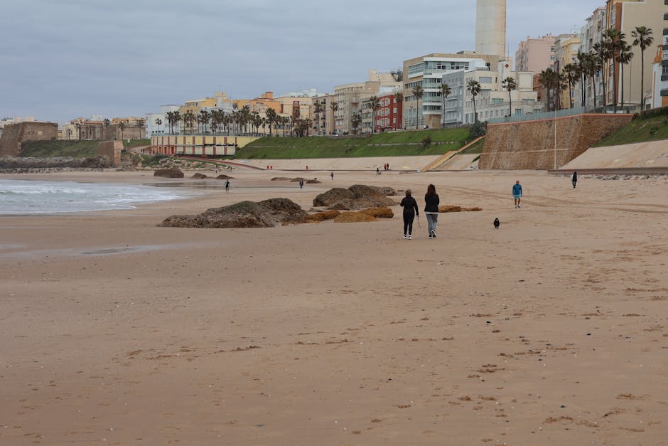 A serene beachfront scene in Cádiz, with ancient city walls and people strolling along the shore.