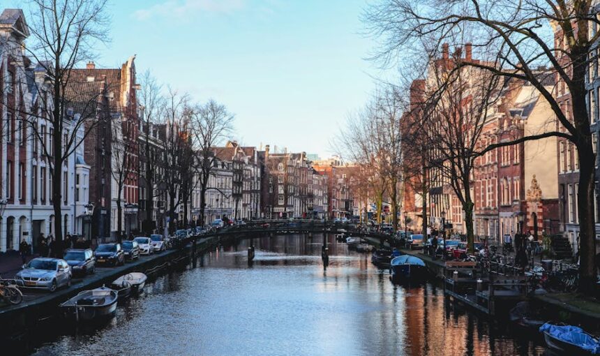 Vista panorâmica de um canal de Amesterdão ladeado por edifícios históricos, barcos e uma atmosfera tranquila.