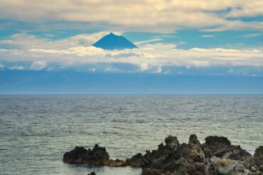 Uma vista serena do mar com um pico vulcânico a emergir por cima das nuvens nos Açores.