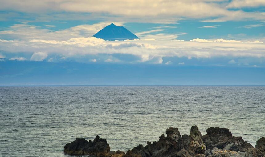 Uma vista serena do mar com um pico vulcânico a emergir por cima das nuvens nos Açores.