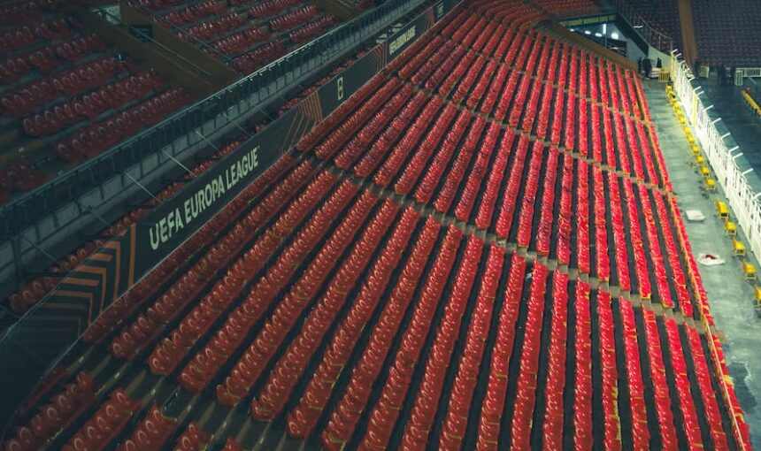 Filas de assentos vermelhos vazios num estádio da Liga Europa da UEFA, capturadas de cima.