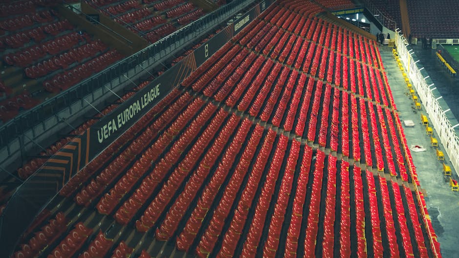 Filas de assentos vermelhos vazios num estádio da Liga Europa da UEFA, capturadas de cima.