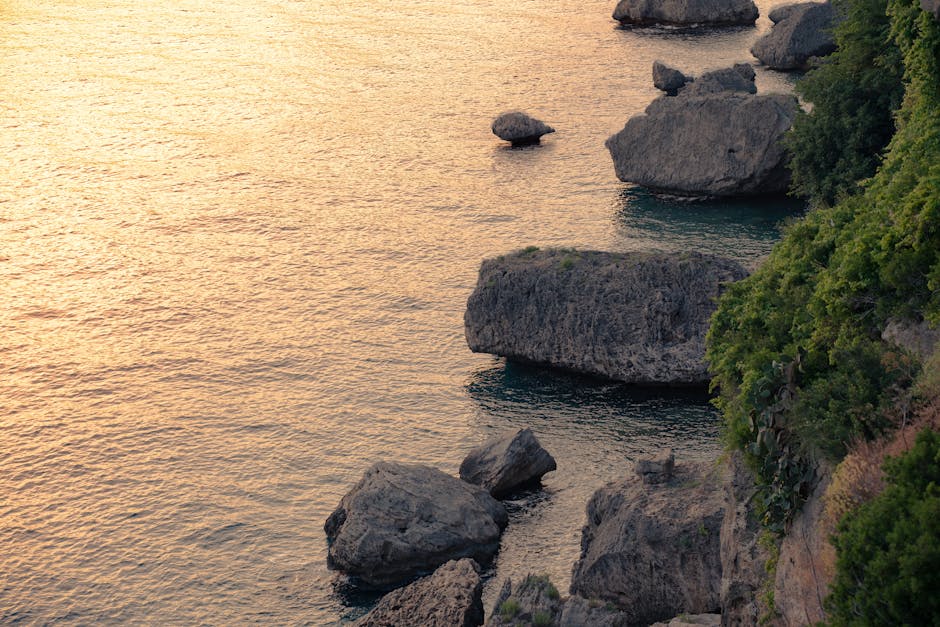 Vista dramática de costa rochosa ao pôr do sol com tons dourados no oceano.