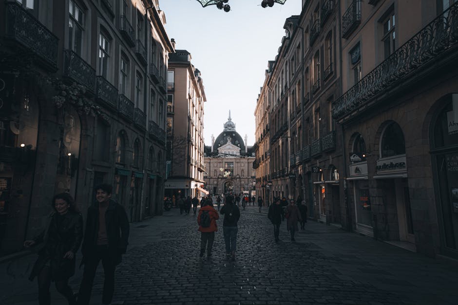 Rua de calçada com arquitetura histórica e pedestres ao anoitecer.