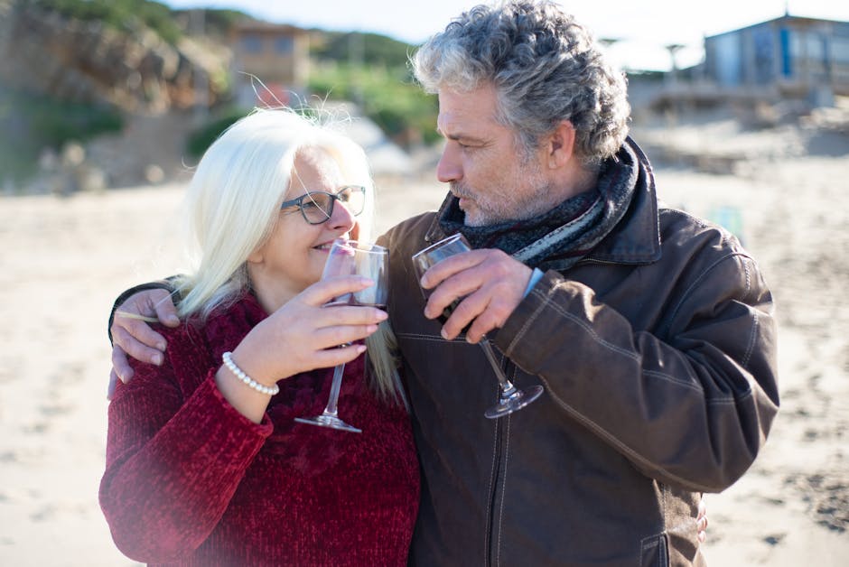 Casal sénior feliz a partilhar vinho numa praia de areia em Portugal.