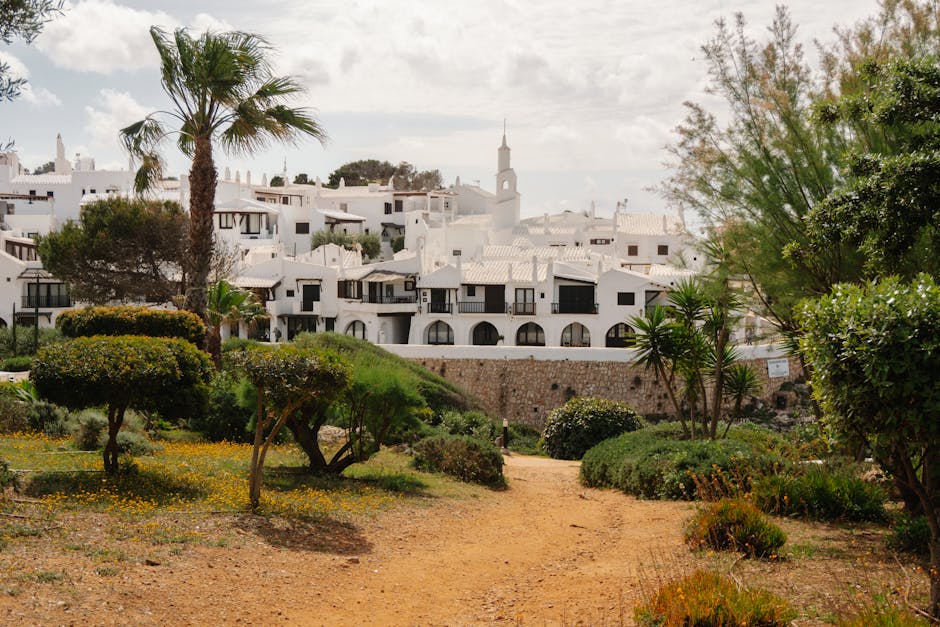 Arquitetura branca encantadora em Ciutadella de Menorca com vegetação luxuriante e palmeiras em primeiro plano.