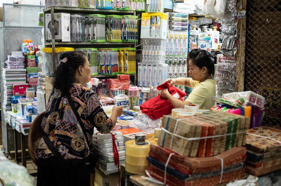 Mulheres a interagir numa loja movimentada do Mercado Dong Xuan, repleta de artigos para o lar em Hanói, Vietname.