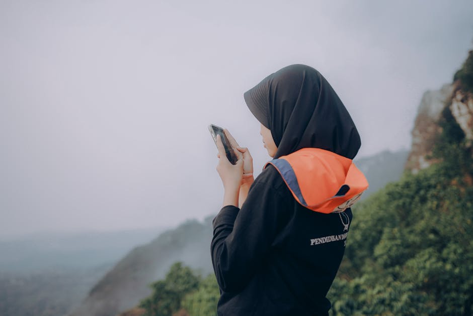 Uma mulher de hijab está ao ar livre, a usar um smartphone nas montanhas da Indonésia.