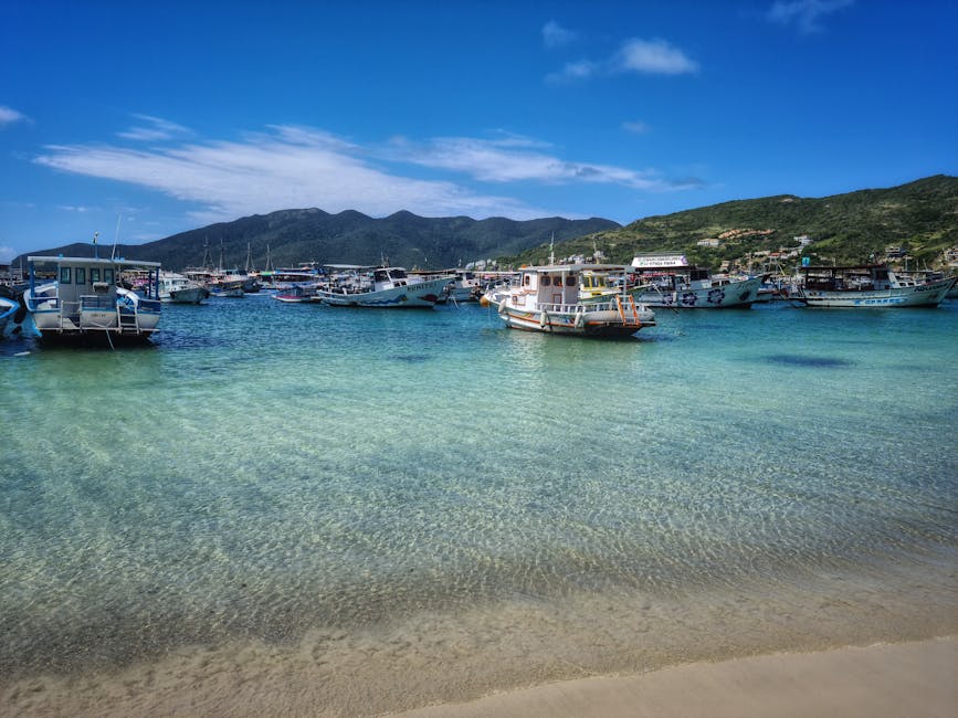 Barcos a flutuar nas águas azul-turquesa de Arraial do Cabo, Brasil, sob um céu azul brilhante.