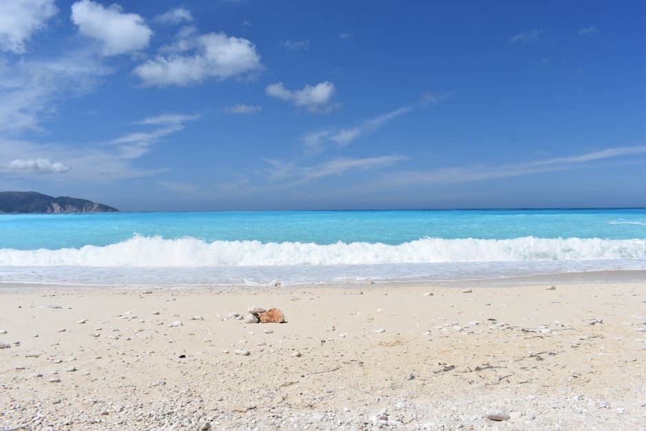 Vista serena da praia em Myrtos Beach, Kefalonia, Grécia, com céu azul límpido e águas azul-turquesa.