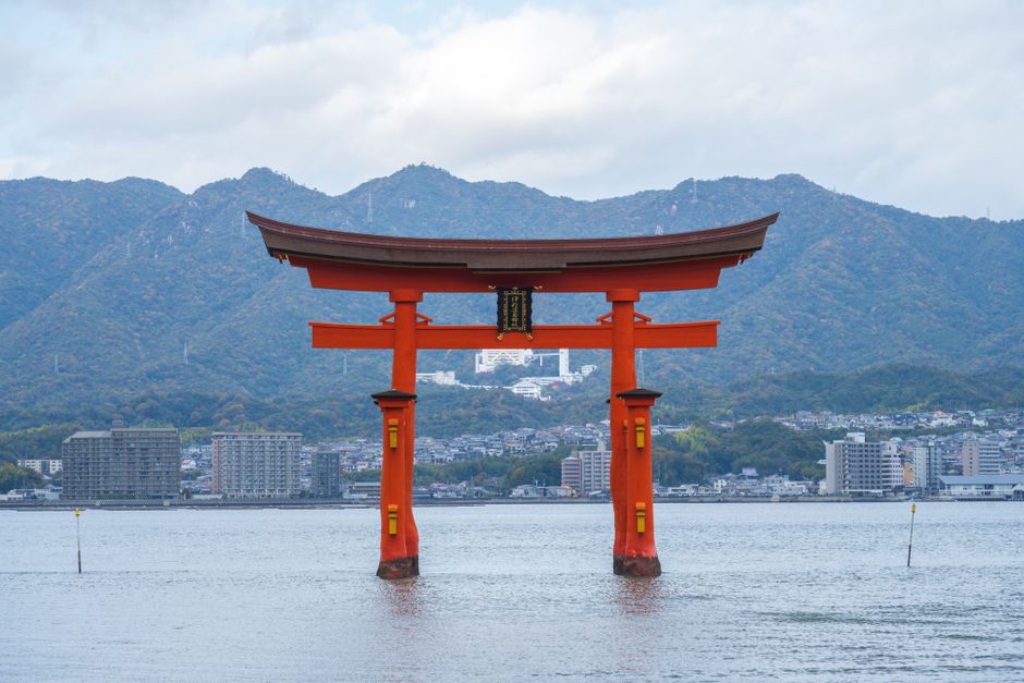 Vista panorâmica do portão Torii flutuante no Santuário de Itsukushima, no Japão, com montanhas e mar.