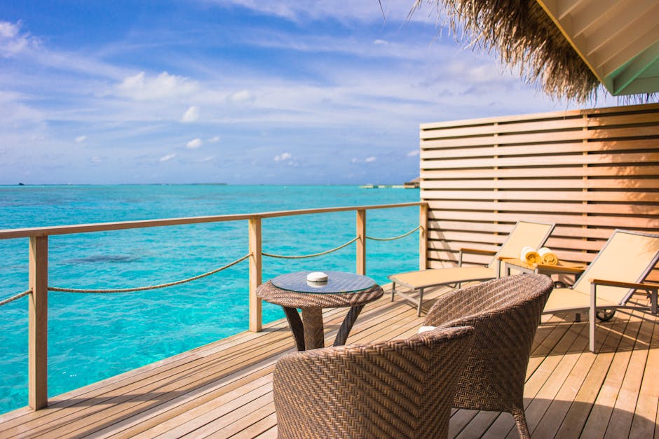 Varanda relaxante à beira-mar com cadeiras e mesa de vime, com vista para águas azul-turquesa sob um céu azul.