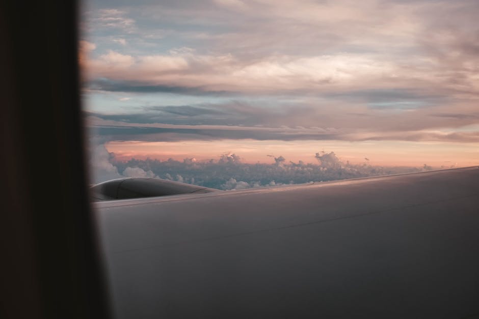 Vista da janela de um avião, mostrando a asa e céus serenos ao pôr do sol acima das nuvens.