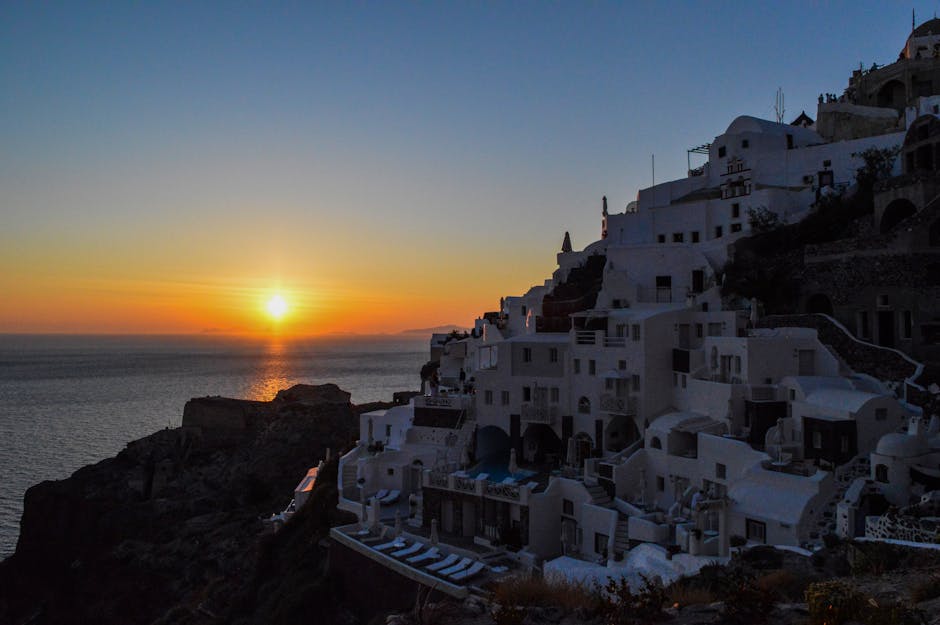Vista deslumbrante das casas brancas no topo da falésia de Santorini, contra um pôr do sol vibrante sobre o mar.