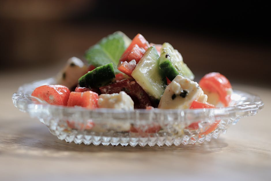 Uma salada mista vibrante com queijo feta, pepinos e tomates numa travessa de vidro.