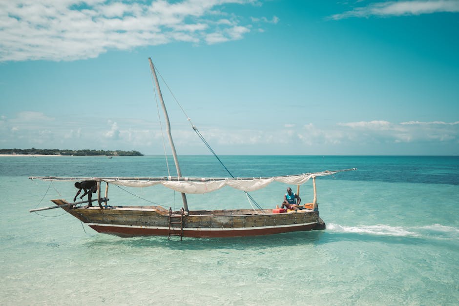 Dois pescadores locais navegam num dhow tradicional nas águas cristalinas de Zanzibar, sob um céu azul brilhante.