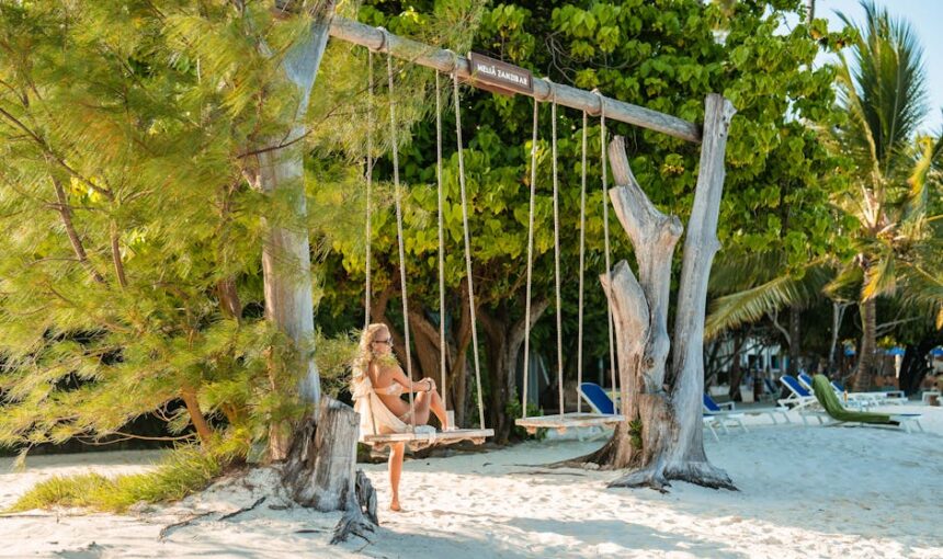 Mulher a desfrutar de um dia soalheiro num baloiço de praia sob coqueiros em Zanzibar.
