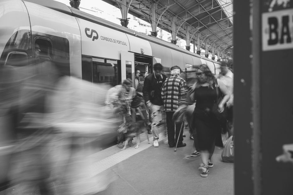 Uma cena a preto e branco de passageiros numa estação de comboios de Lisboa, a mostrar o movimento urbano.