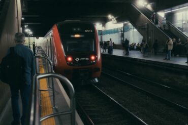 Um elegante comboio vermelho numa plataforma movimentada de estação ferroviária, à noite.