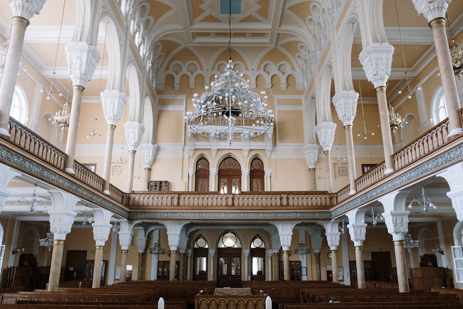 Vista cativante do interior de uma sinagoga histórica com arquitetura ornamentada, candelabros e arcos.