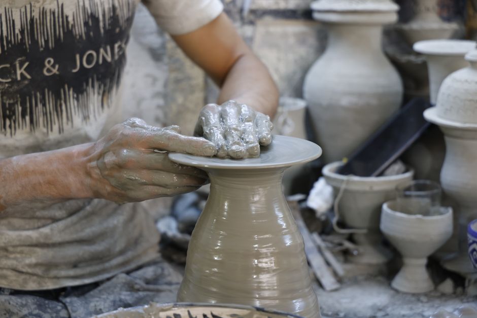 Artesão a moldar argila num torno de oleiro, realçando o trabalho artesanal e a arte envolvida.