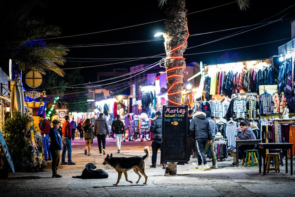 Mercado noturno vibrante ao ar livre com bancas iluminadas, compradores e vendedores.