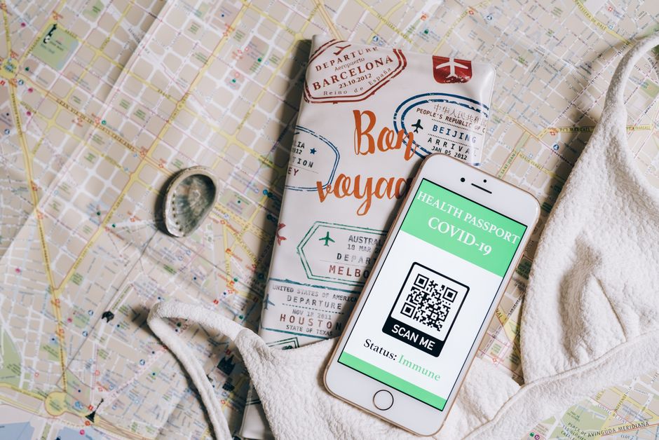 Smartphone a exibir um passaporte de saúde com código QR sobre um mapa de viagens e capa de passaporte.