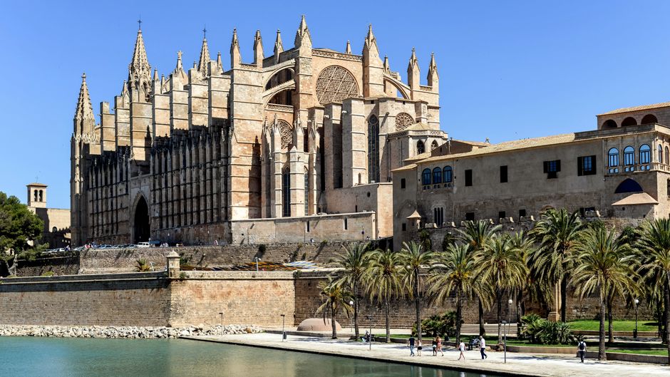 Arquitetura gótica da Catedral de La Seu em Palma, Maiorca, com palmeiras sob um céu azul límpido.