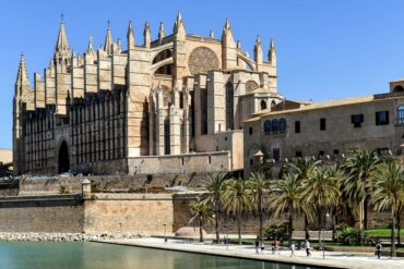 Arquitetura gótica da Catedral de La Seu em Palma, Maiorca, com palmeiras sob um céu azul límpido.