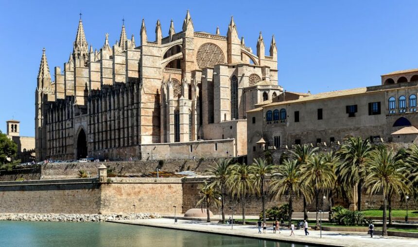 Arquitetura gótica da Catedral de La Seu em Palma, Maiorca, com palmeiras sob um céu azul límpido.