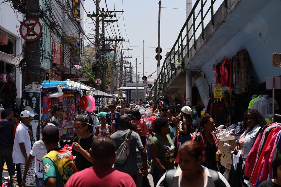Mercado de rua movimentado em São Paulo com pessoas diversas e bancas coloridas.