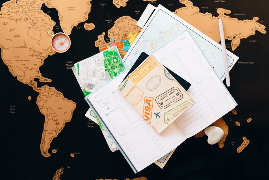 Uma composição de cima para baixo de artigos de planeamento de viagens sobre um mapa, com uma bússola, um caderno e um guia para entusiastas de viagens.