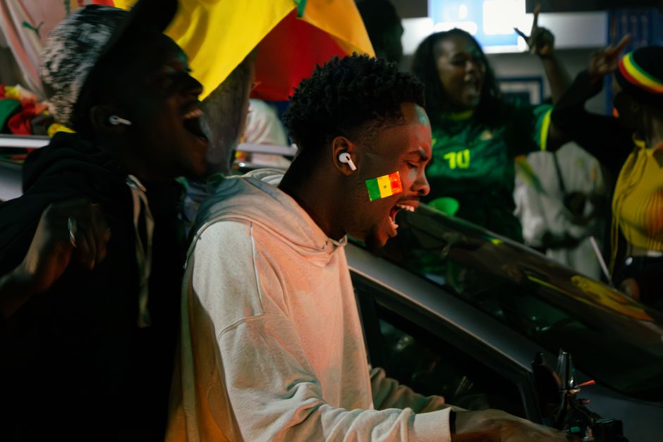 Um grupo a celebrar exuberantemente com a bandeira senegalesa pintada no rosto de um homem, capturando a energia vibrante da rua.