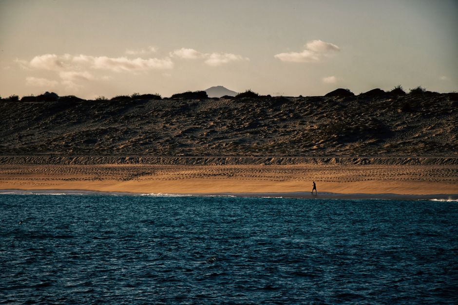 Uma cena de praia tranquila com um caminhante ao longe em Cabo San Lucas, capturada durante um pôr do sol deslumbrante.
