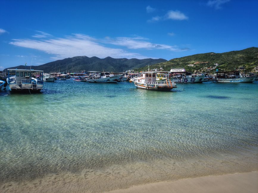 Barcos a flutuar nas águas azul-turquesa de Arraial do Cabo, Brasil, sob um céu azul brilhante.