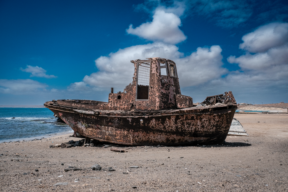 Um barco enferrujado e abandonado nas praias arenosas de Pedra de Lume, Ilha do Sal, sob um céu azul vibrante.