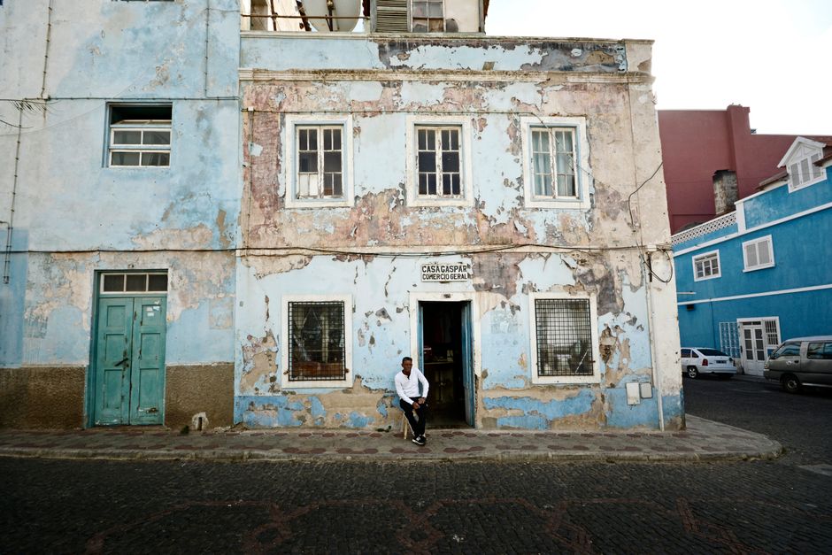 Um edifício desgastado com um homem sentado à porta nas ruas urbanas de Mindelo, Cabo Verde.