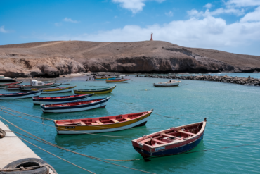 Cena animada de barcos de pesca coloridos ancorados nas águas serenas de Pedra Lume, Sal, Cabo Verde.