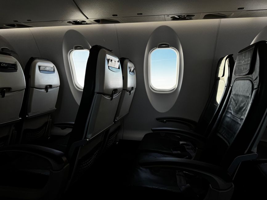 Interior de uma cabine de avião vazia com um céu luminoso visível pela janela.