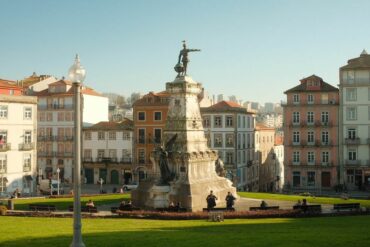 Bela vista de uma estátua numa praça histórica do Porto com arquitetura tradicional.
