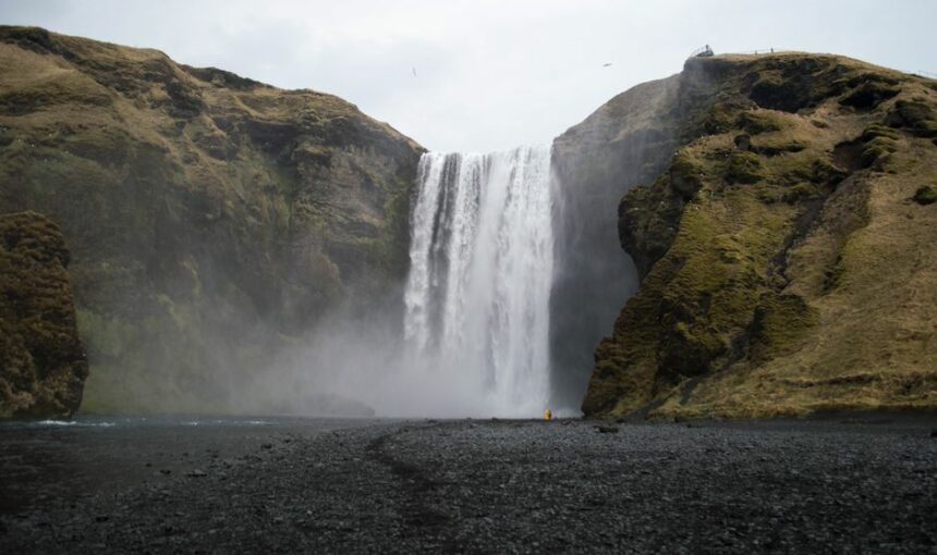 Explore a deslumbrante cascata Skógafoss na Islândia, rodeada por falésias cobertas de musgo e areia negra.