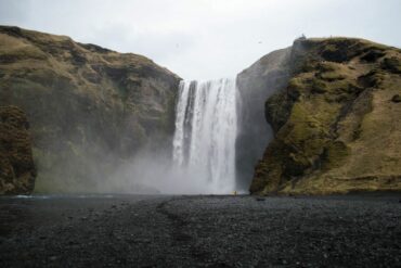 Explore a deslumbrante cascata Skógafoss na Islândia, rodeada por falésias cobertas de musgo e areia negra.