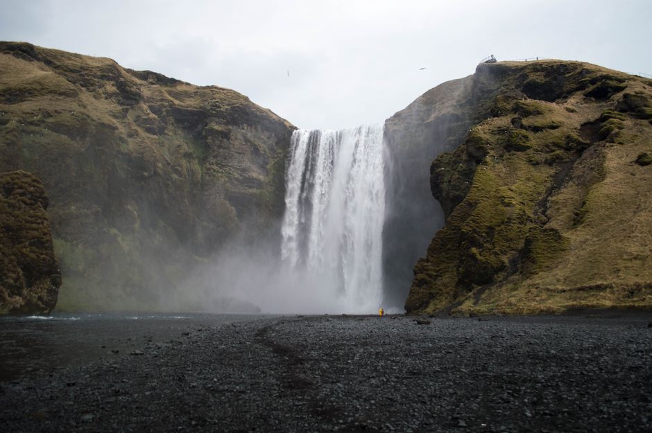 Explore a deslumbrante cascata Skógafoss na Islândia, rodeada por falésias cobertas de musgo e areia negra.